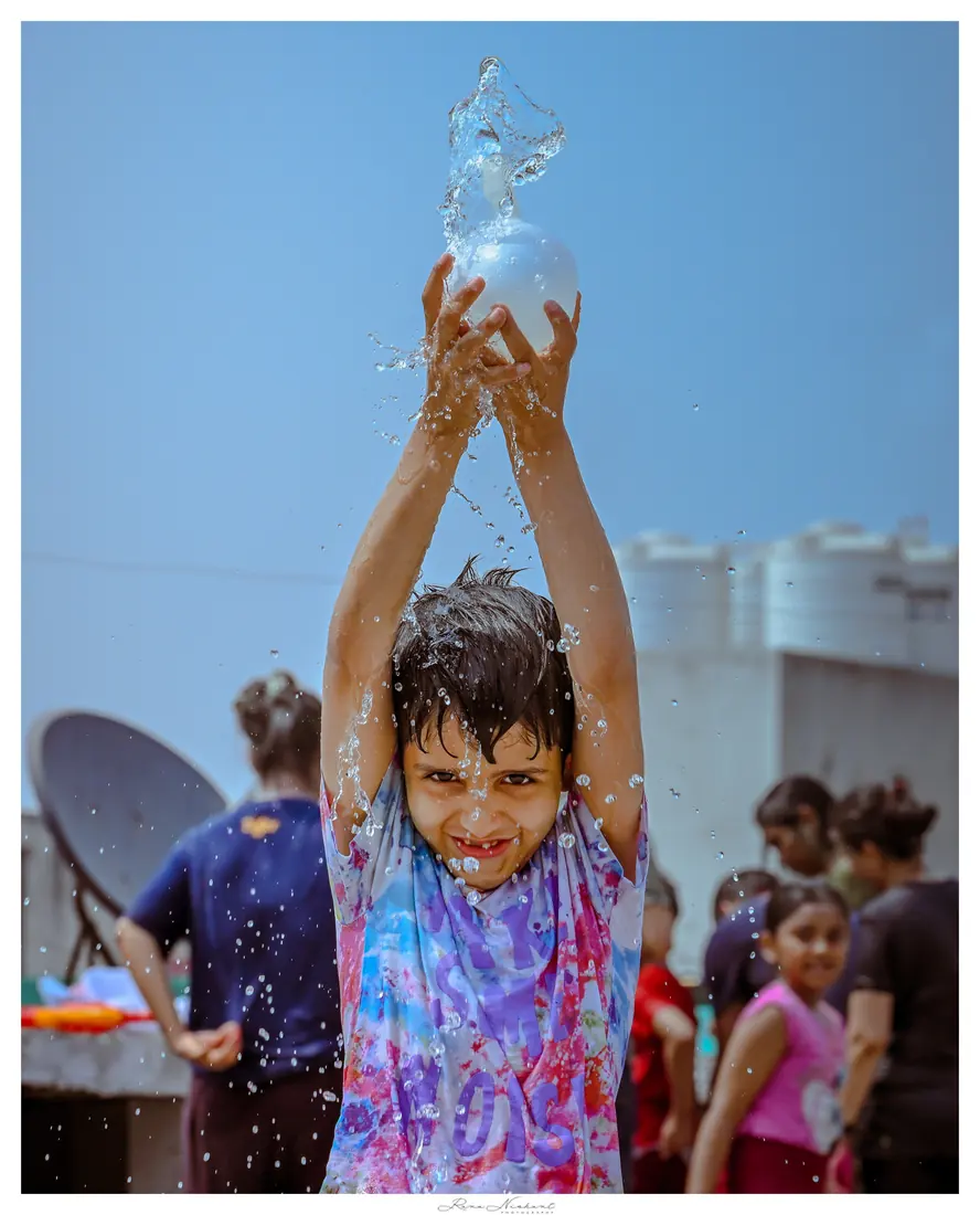 A child lifting a bursting water balloon overhead during Holi